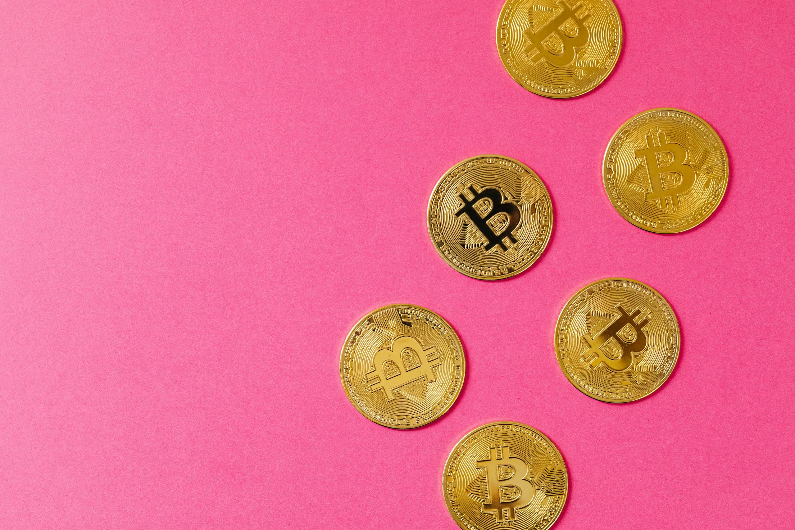 Gold Bitcoin coins on a vibrant pink surface, representing cryptocurrency and blockchain investment.